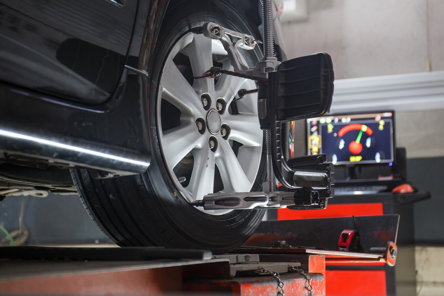 Close-up of a vehicle's wheel on an alignment rack with a digital reading in the background