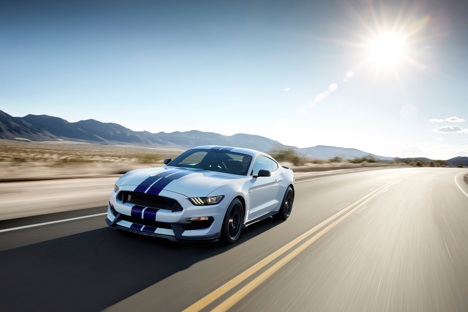 2015 Ford Shelby GT350 Mustang in white with blue stripes driving on a deserted road