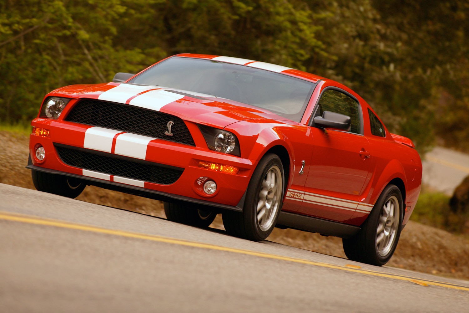 2007 Ford Mustang Shelby GT500 in red with white stripes driving on a back road