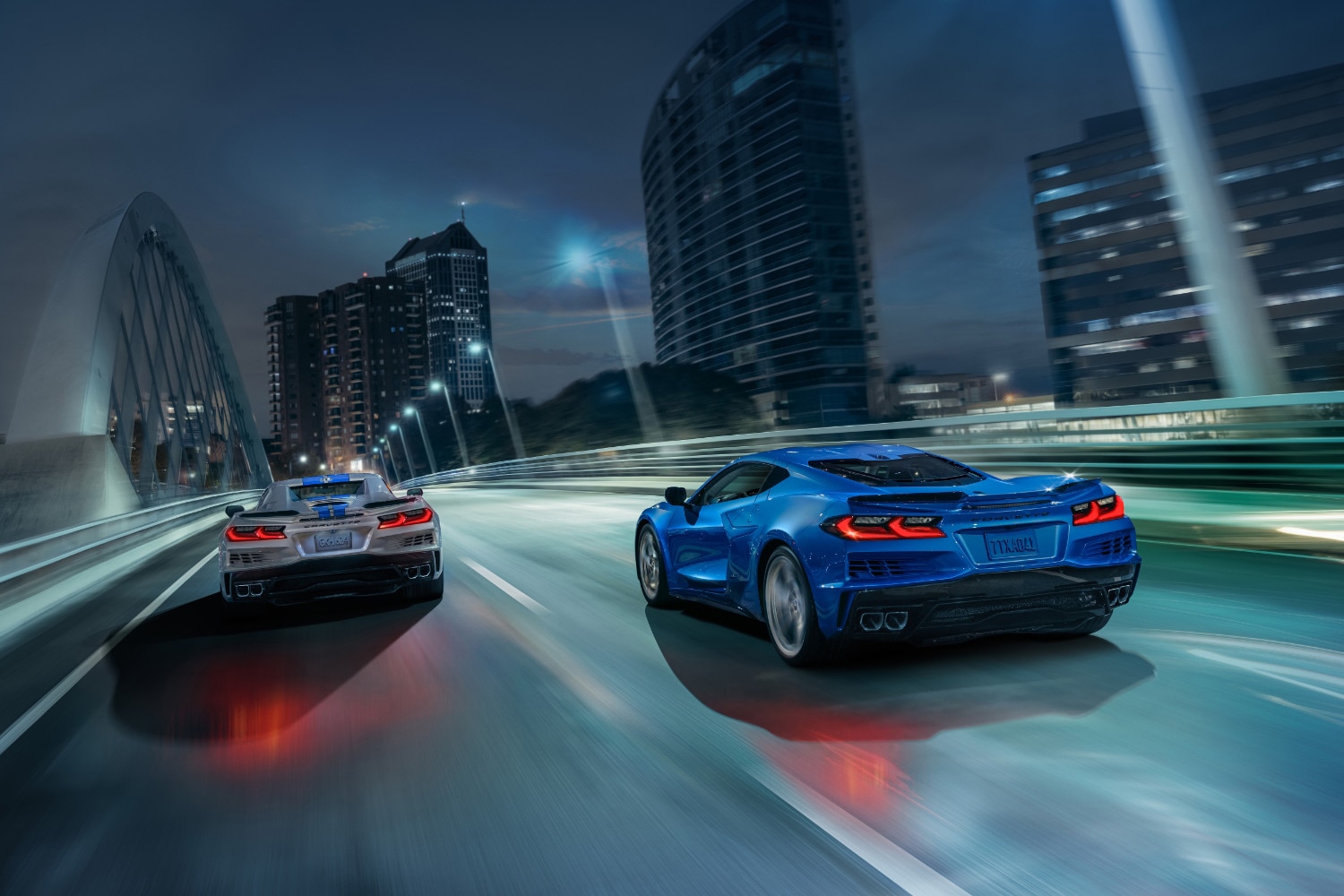 2024 Chevrolet Corvette E-Ray, one in Silver Flare with Electric Blue stripes and one in Riptide Blue, rear action shot