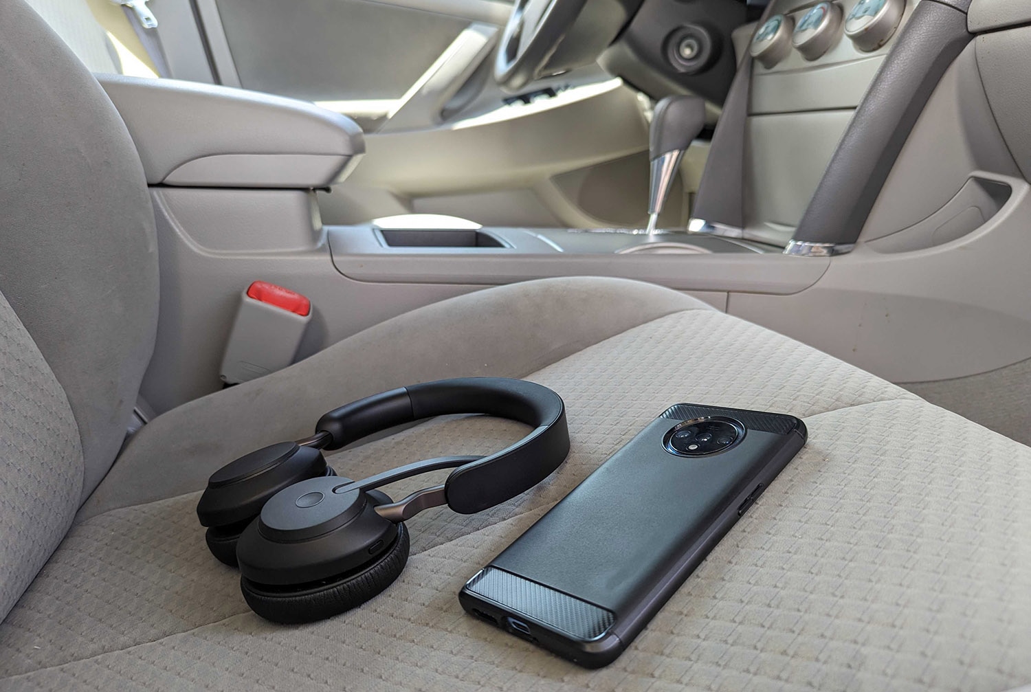 A cell phone and headphones lie on the passenger seat of a vehicle in plain view.