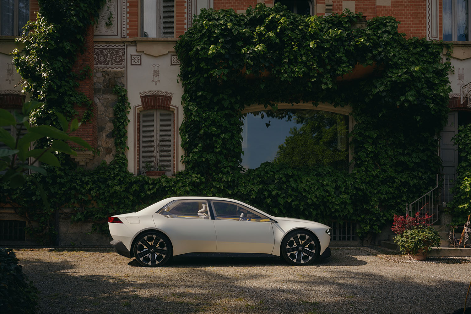 BMW Vision Neue Klasse in Joyous Bright off-white parked outside a lush villa, side view