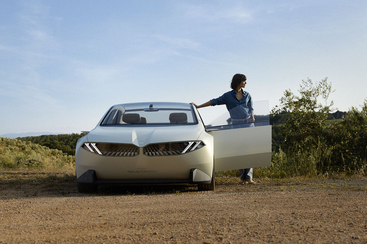 BMW Vision Neue Klasse in Joyous Bright off-white, front view, with woman standing in the opening of the left-front door