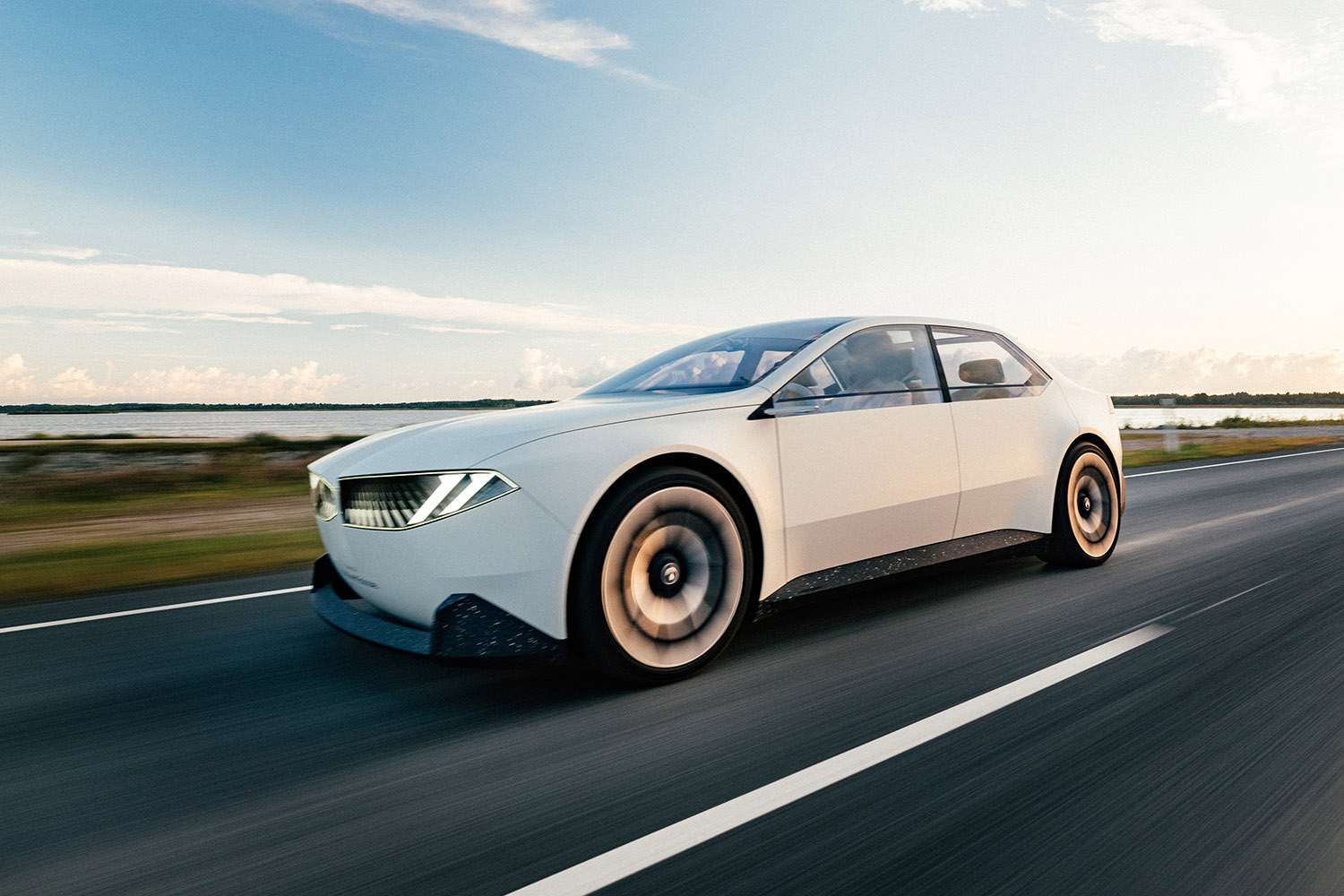 BMW Vision Neue Klasse in Joyous Bright off-white driving along a lake-adjacent road