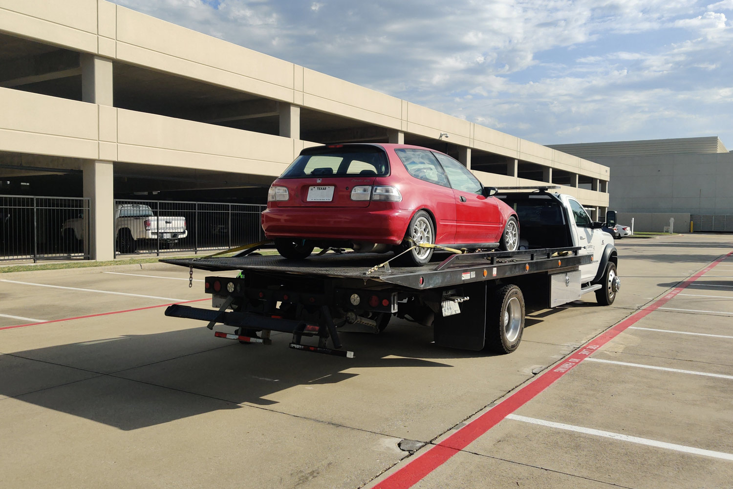 A red Honda Civic is secured on the back of a flatbed tow truck