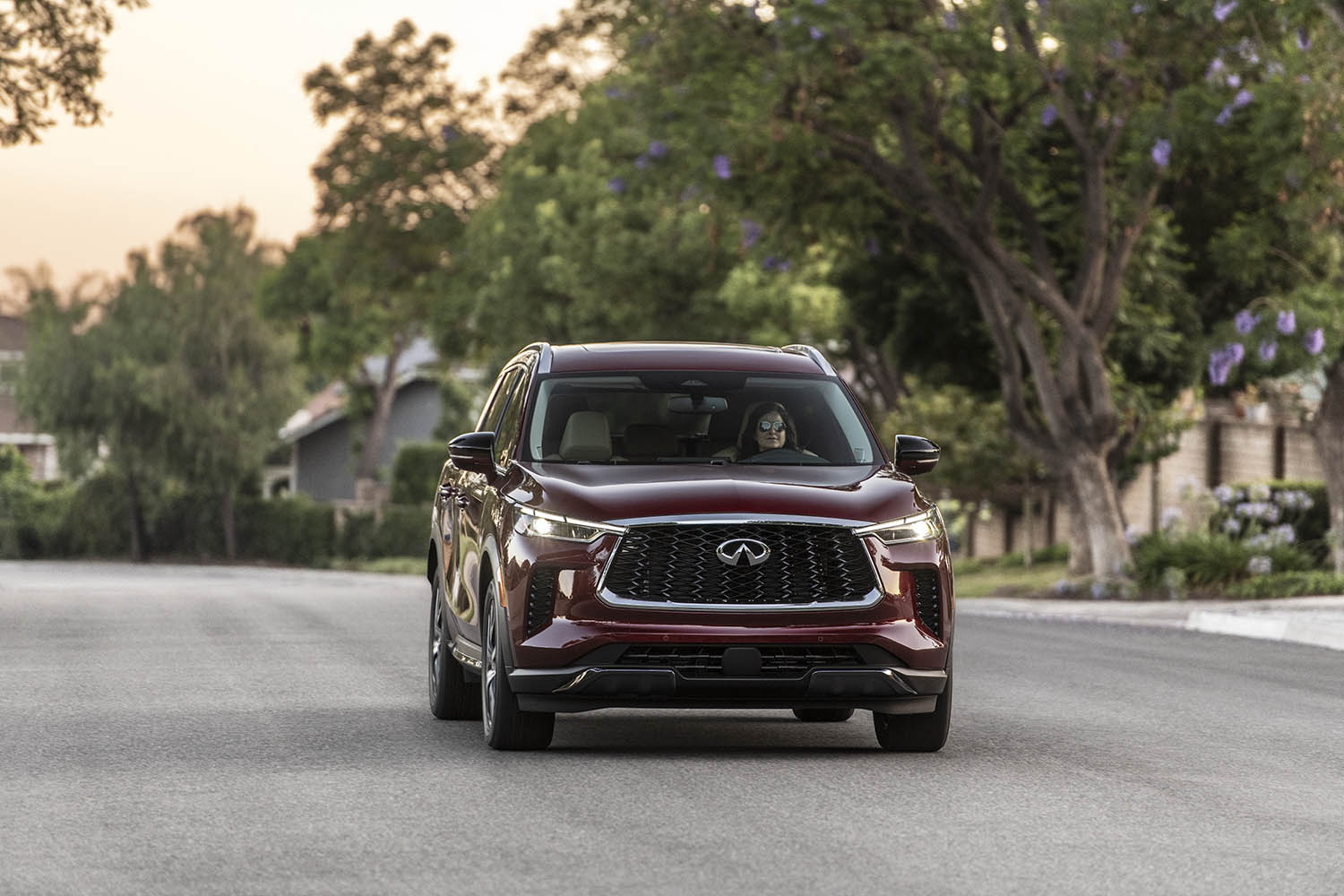2023 Infiniti QX60 in dark red driving on a residential street
