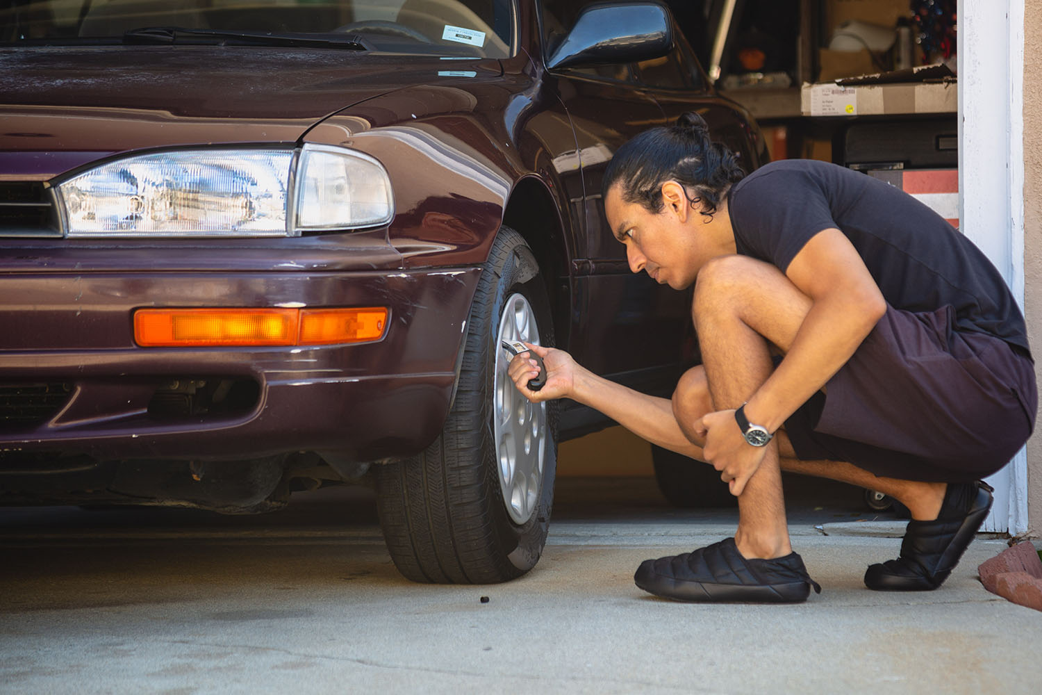 A person checking pressure and wear of a car tire.