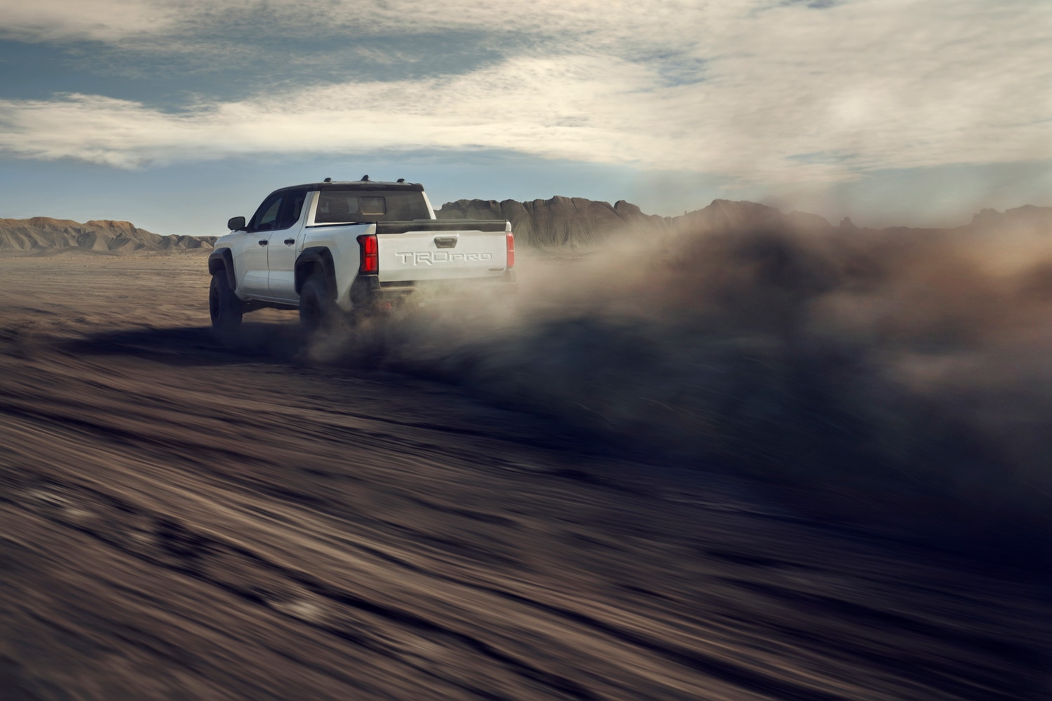 2024 Toyota Tacoma TRD Pro driving fast on dirt with a large dust cloud behind it.
