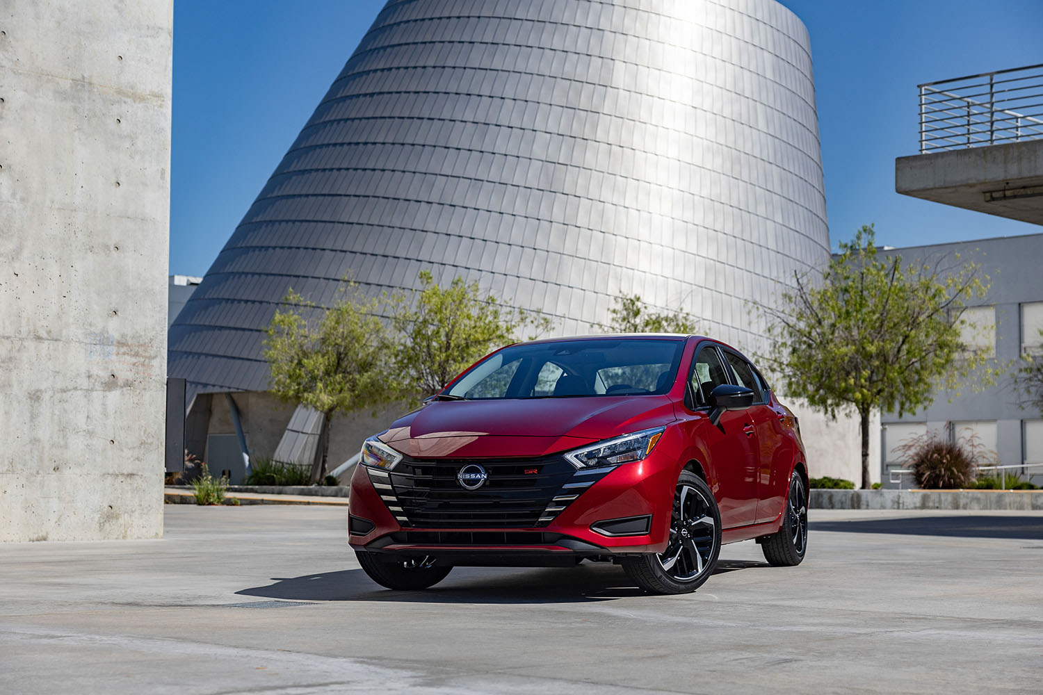 Red Nissan Versa parked in front of metal and concrete structures