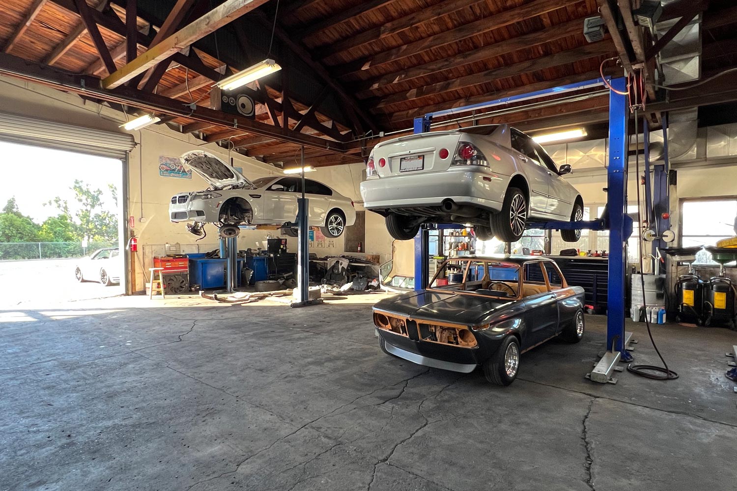Three cars are parked in a repair shop with two raised on vehicle lifts.