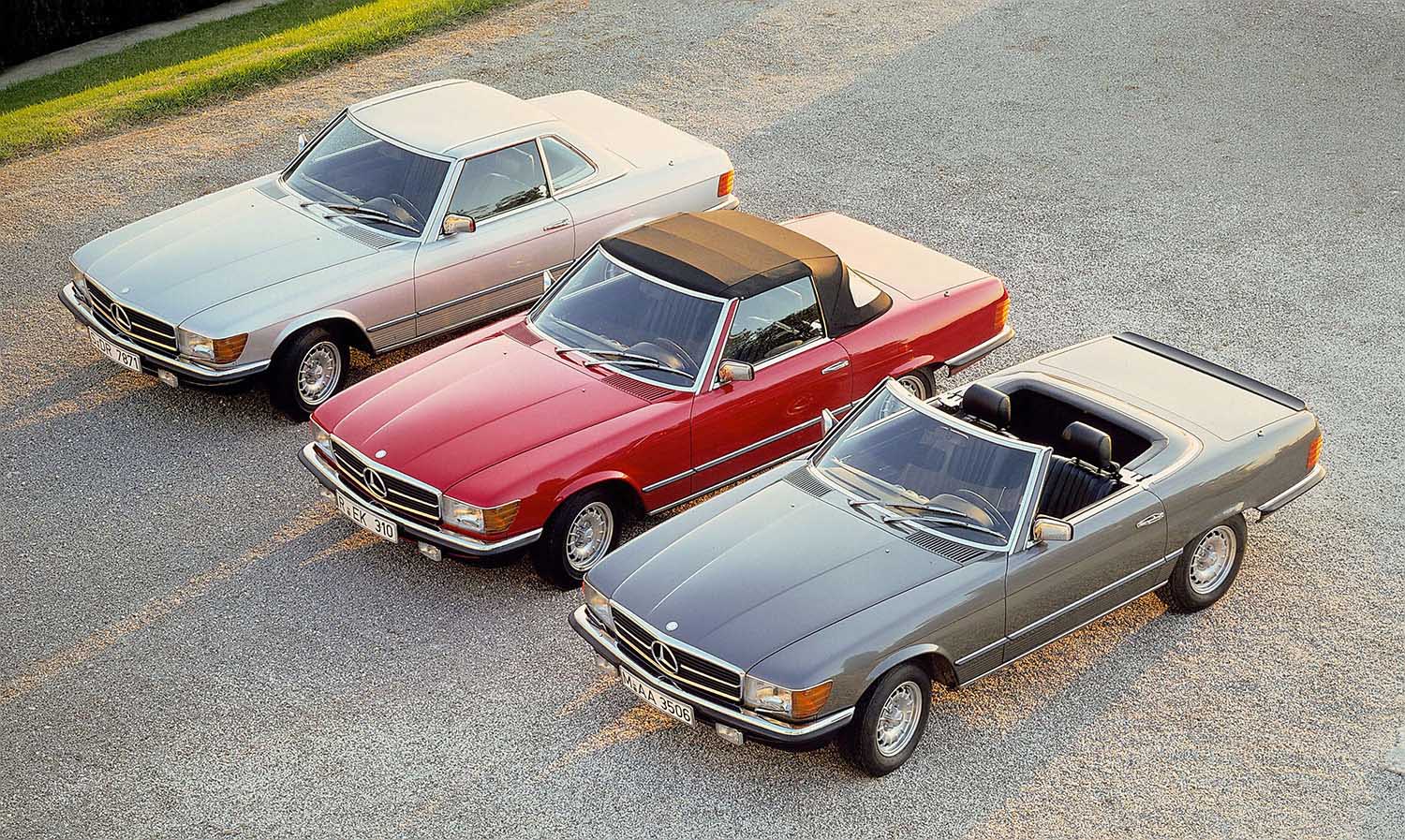 1971 to 1989 (R107) Mercedes-Benz SL-Class trio (from left to right) in silver, red, and gray displaying the hardtop, closed-softtop, and open-top-convertible states of configuration.