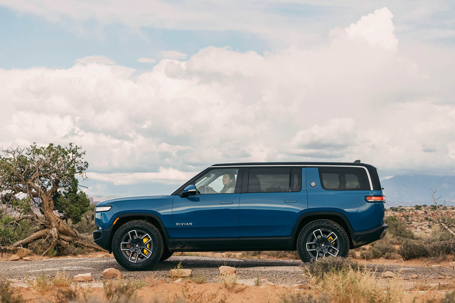 Side view of Rivian R1S in blue-green parked on dirt road