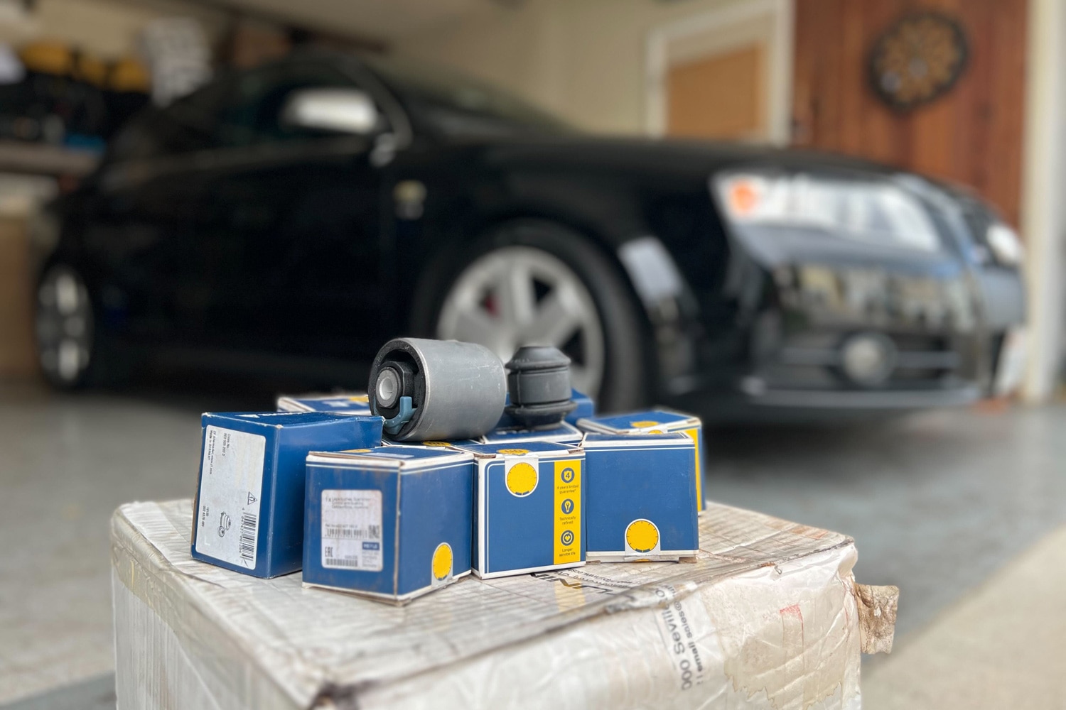  Several suspension bushings and boxes are stacked in front of black car in a garage