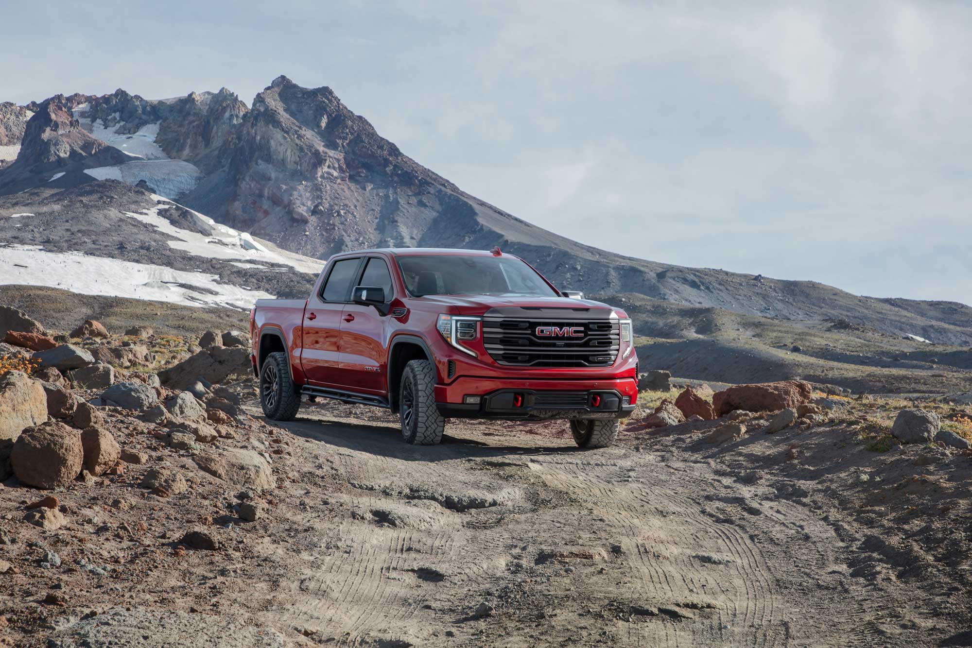 GMC Sierra 1500 in red parked on dirt road with snowy mountain in the background