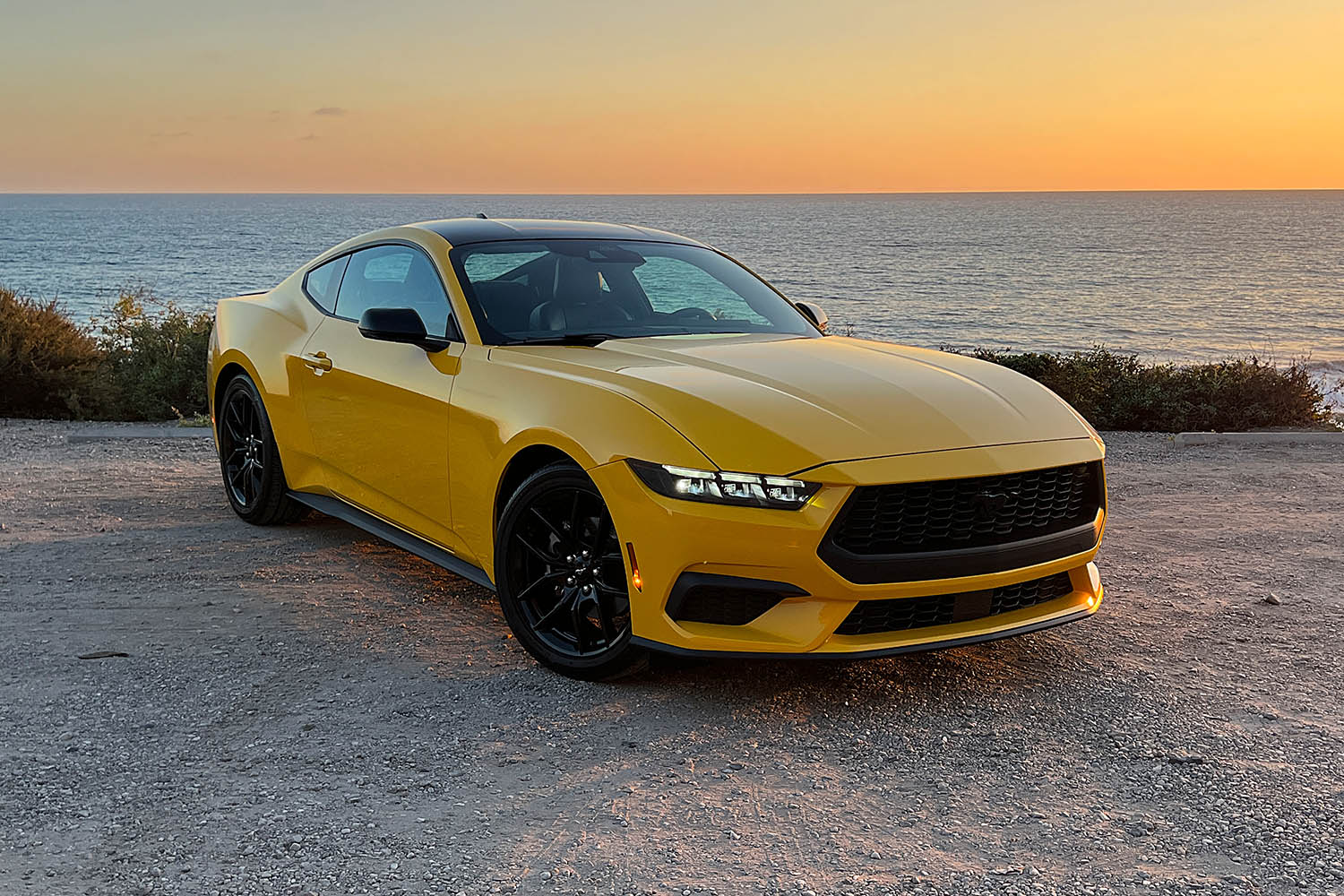 2024 Ford Mustang in Yellow Splash Metallic parked against the Southern California coast at sunset, front-quarter view.