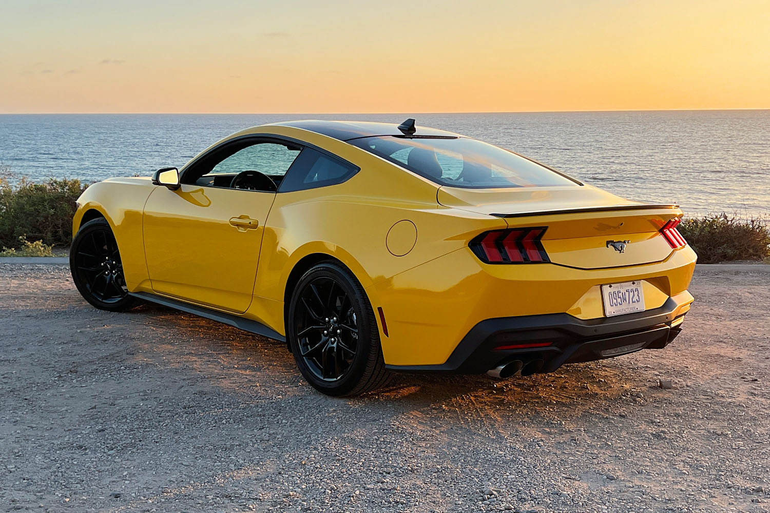  2024 Ford Mustang in Yellow Splash Metallic parked against the Southern California coast at sunset, rear-quarter view.