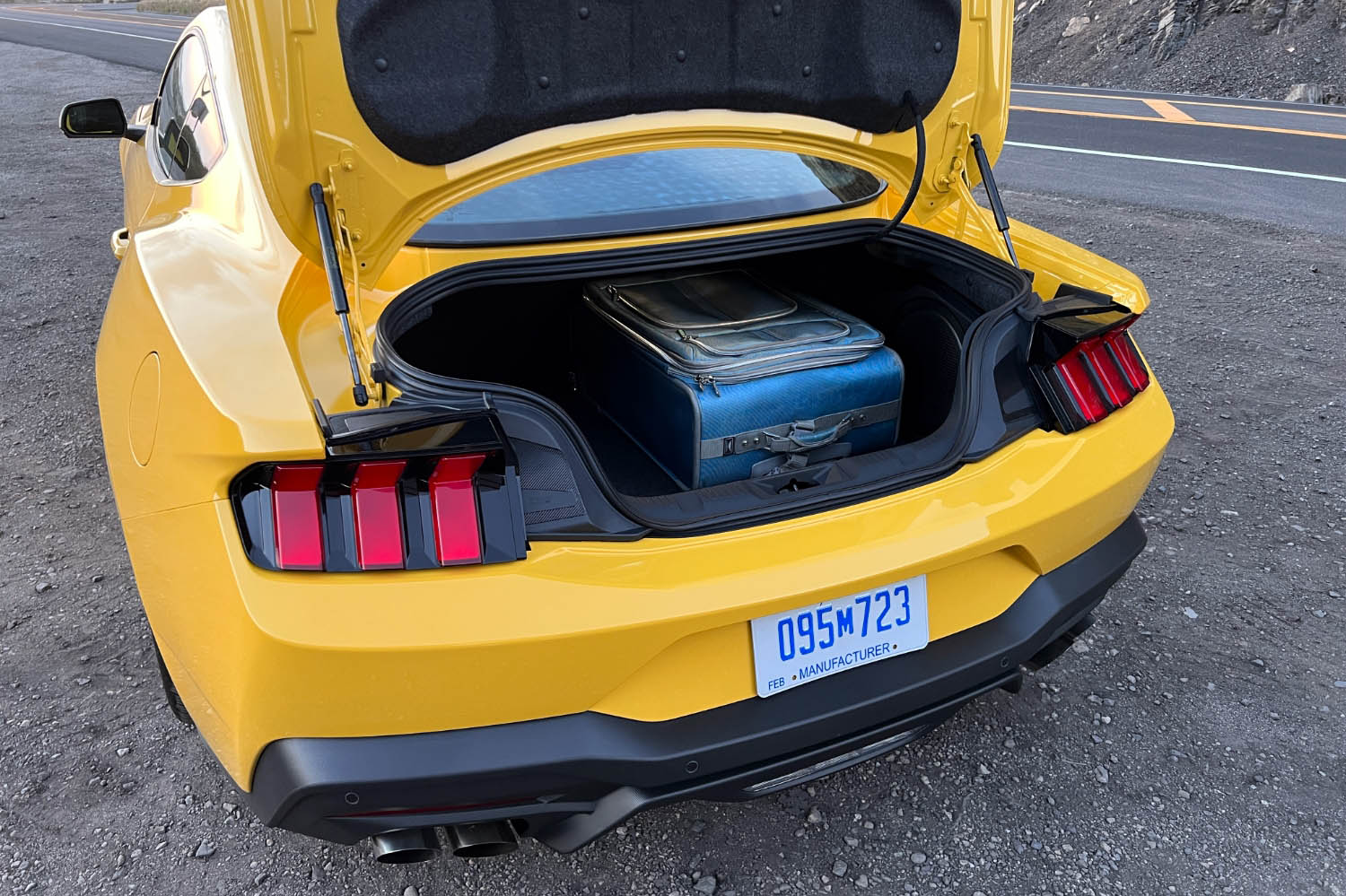 2024 Ford Mustang in yellow with the trunklid open to display the cargo space with carry-on luggage inside.