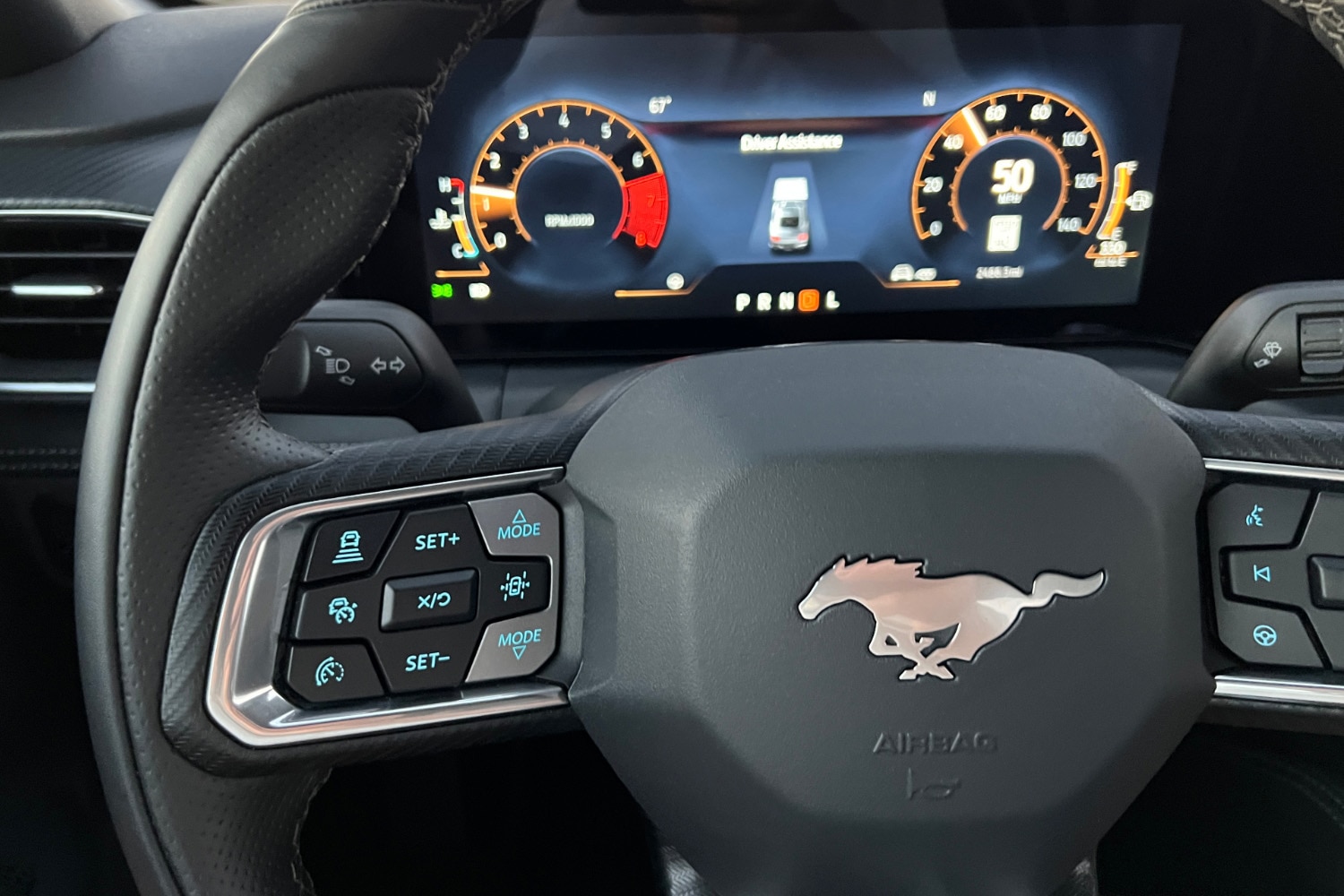  2024 Ford Mustang steering wheel and spoke controls in front of a blurry instrument cluster screen showing its driver-assistance display mode.