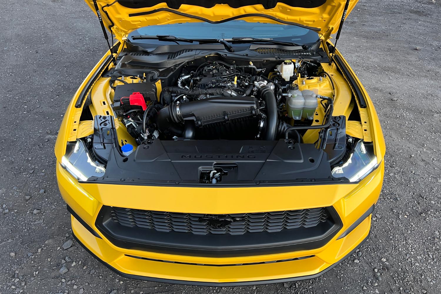 2024 Ford Mustang in yellow with its hood open to display the 2.3-liter turbocharged EcoBoost four-cylinder engine.
