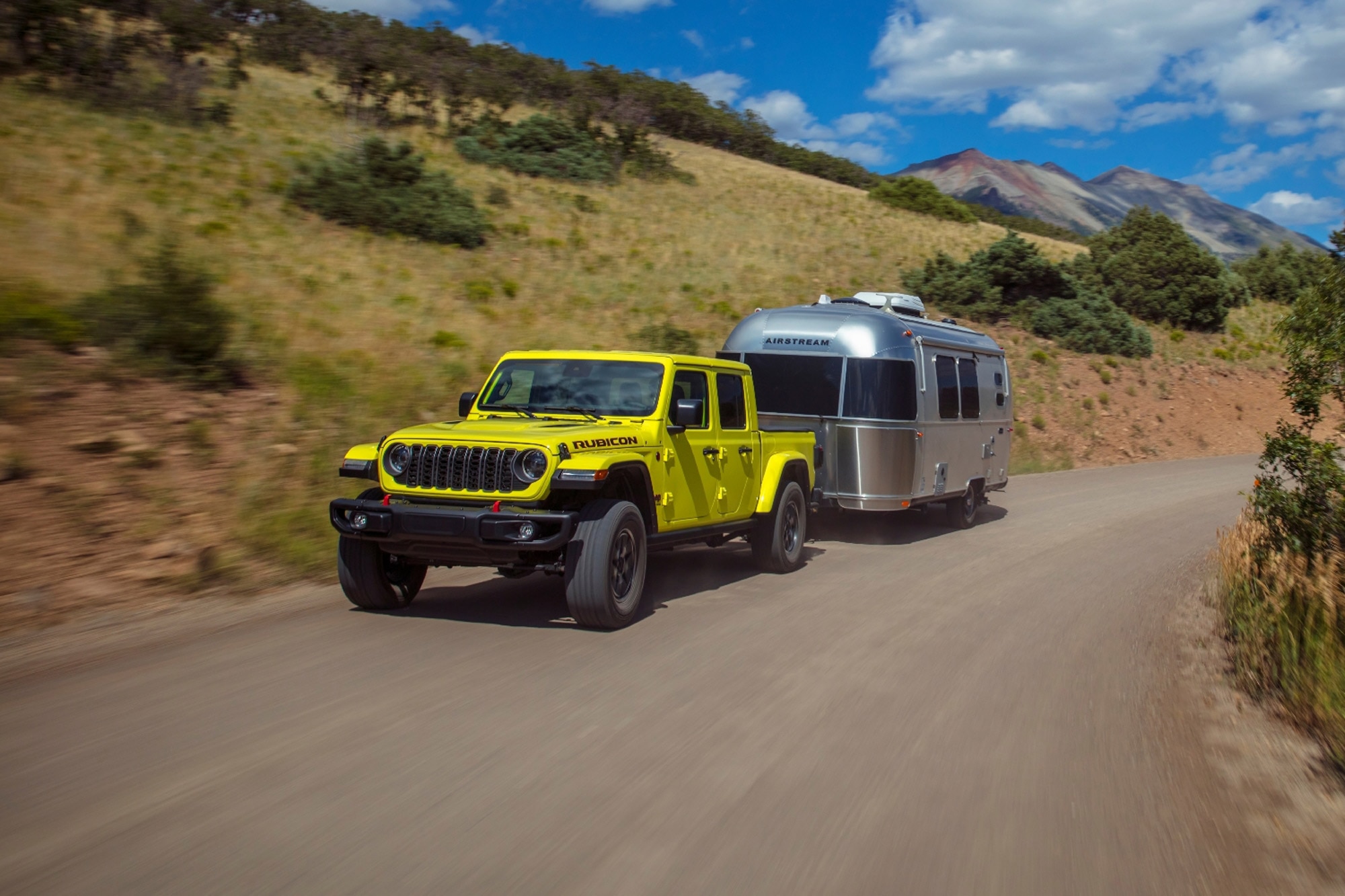 2024 Jeep Gladiator Rubicon in yellow towing gray airstream on the highway