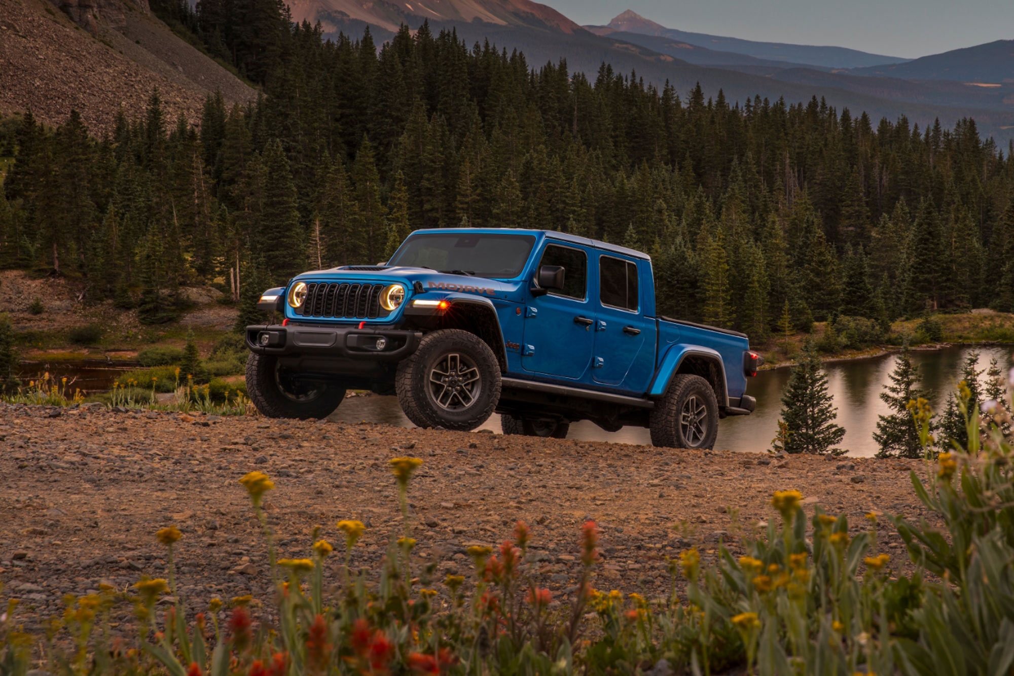 2024 Jeep Gladiator Mojave in blue parked in the field next to the lake and mountains