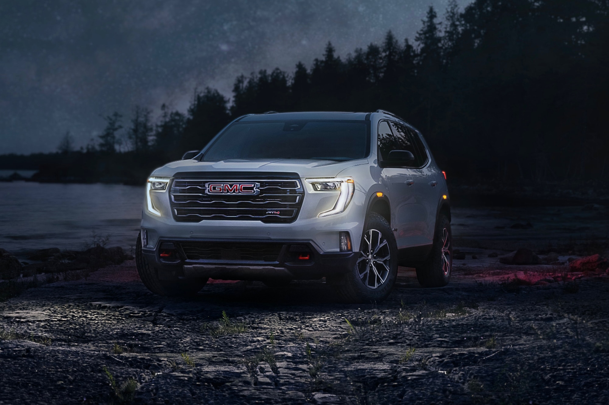 2024 GMC Acadia AT4 in white parked by the ocean and forest at night