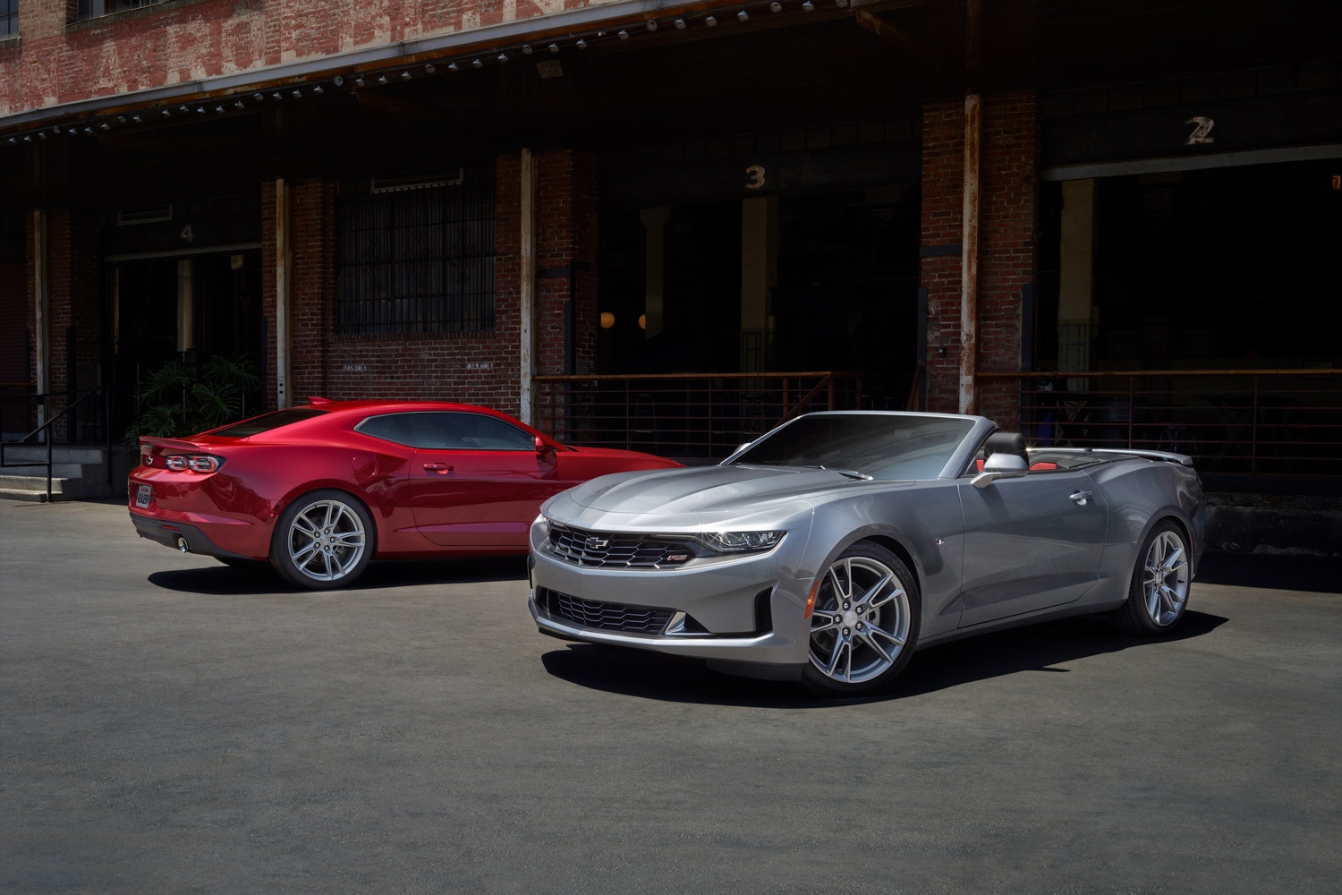 Side view of a red 2023 Chevrolet Camaro parked next to a silver 2023 Chevrolet Camaro convertible