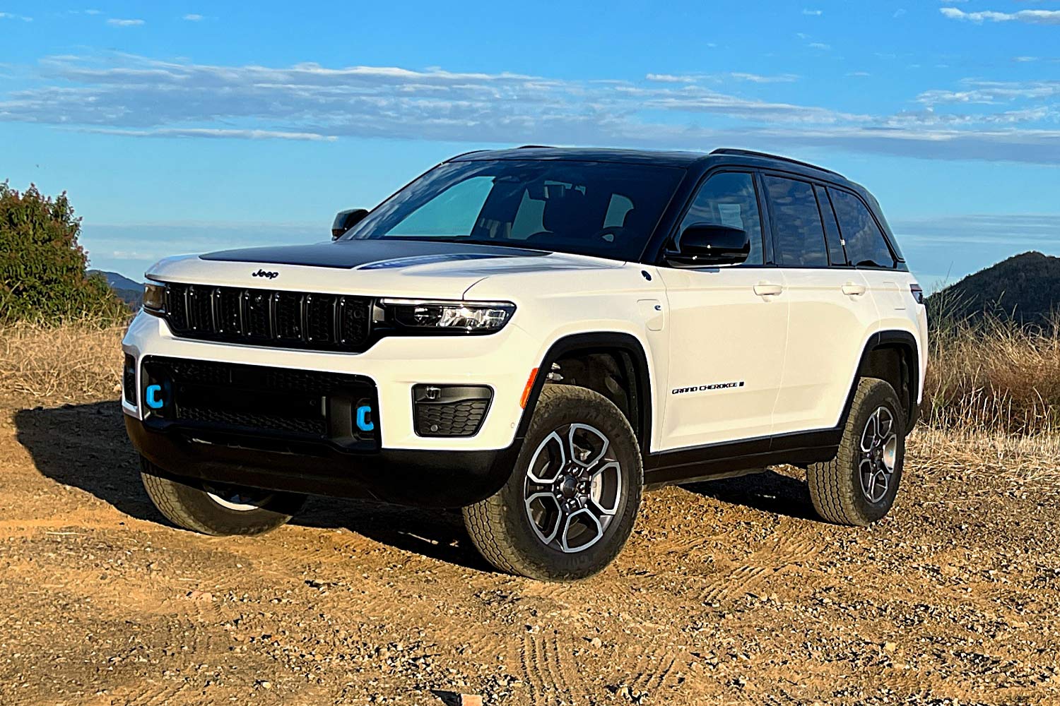 White 2023 Jeep Grand Cherokee 4xe Trailhawk parked on dirt in hills.