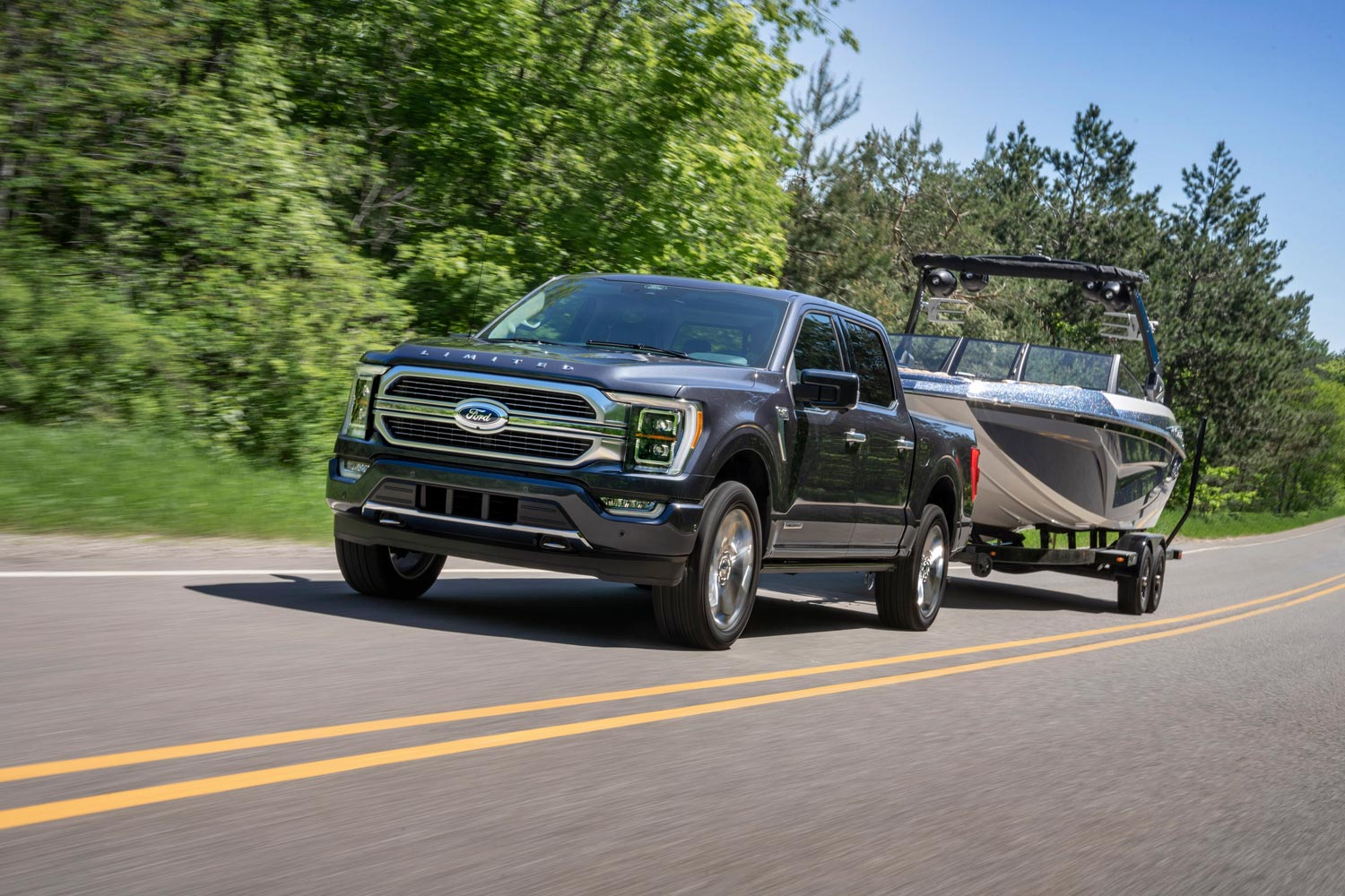 Ford F-150 towing a trailer and a ski boat on a two-lane road.