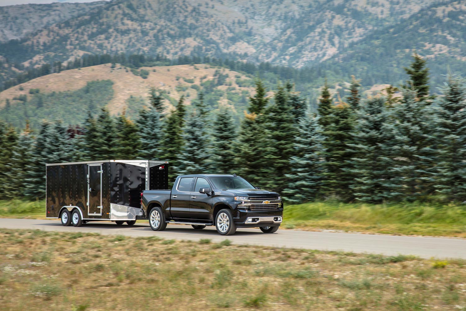 2023 Chevrolet Silverado towing an enclosed utility trailer along forest road.