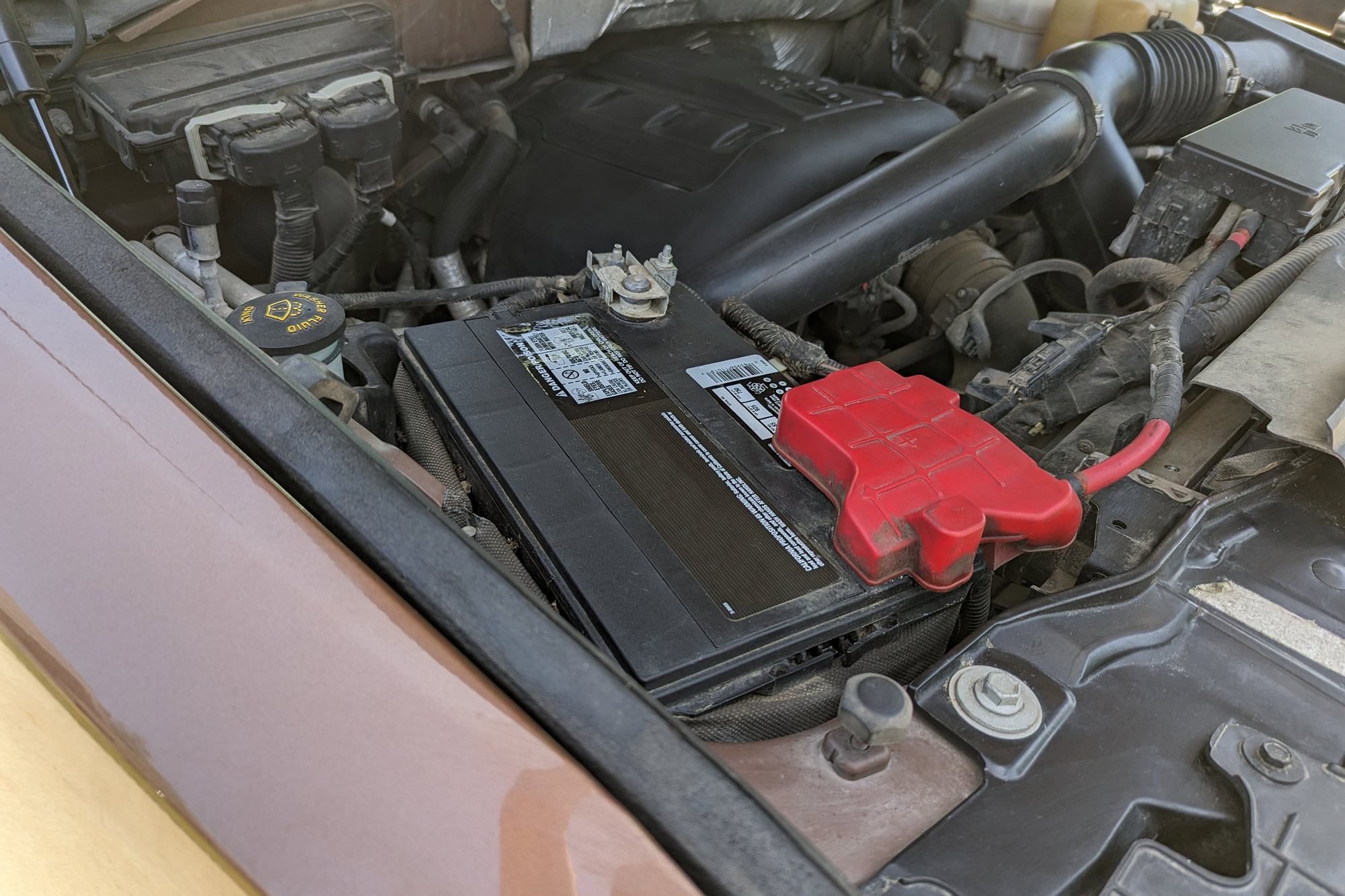 Close-up view of a 12-volt car battery in an engine bay of a brown pickup truck.