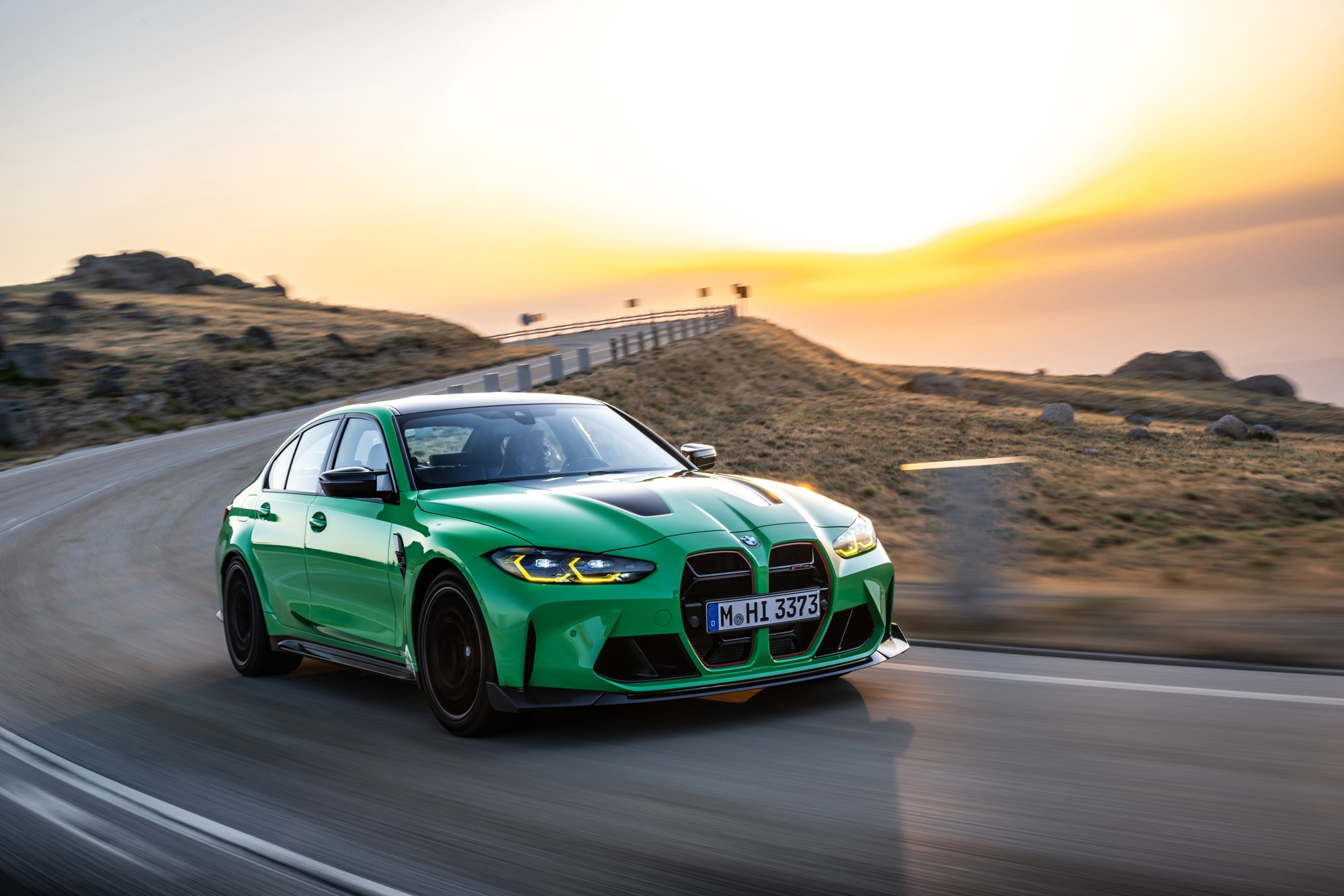 Green 2023 BMW M3 driving on scenic road.