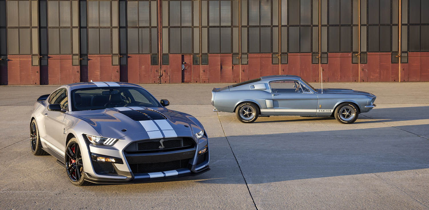 2022 Ford Mustang Shelby GT500 in gray with white racing stripes parked beside a vintage Shelby GT500 Mustang in light blue