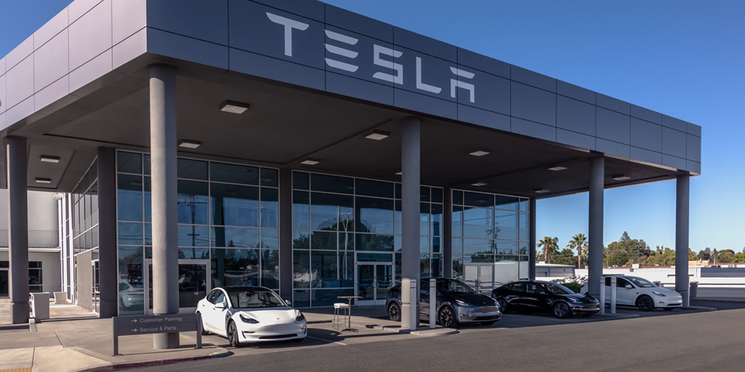 Exterior of Tesla building with four Tesla vehicles parked outside.