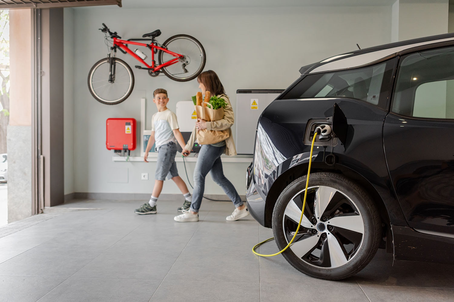 Parent and child in garage next to plugged-in electric vehicle