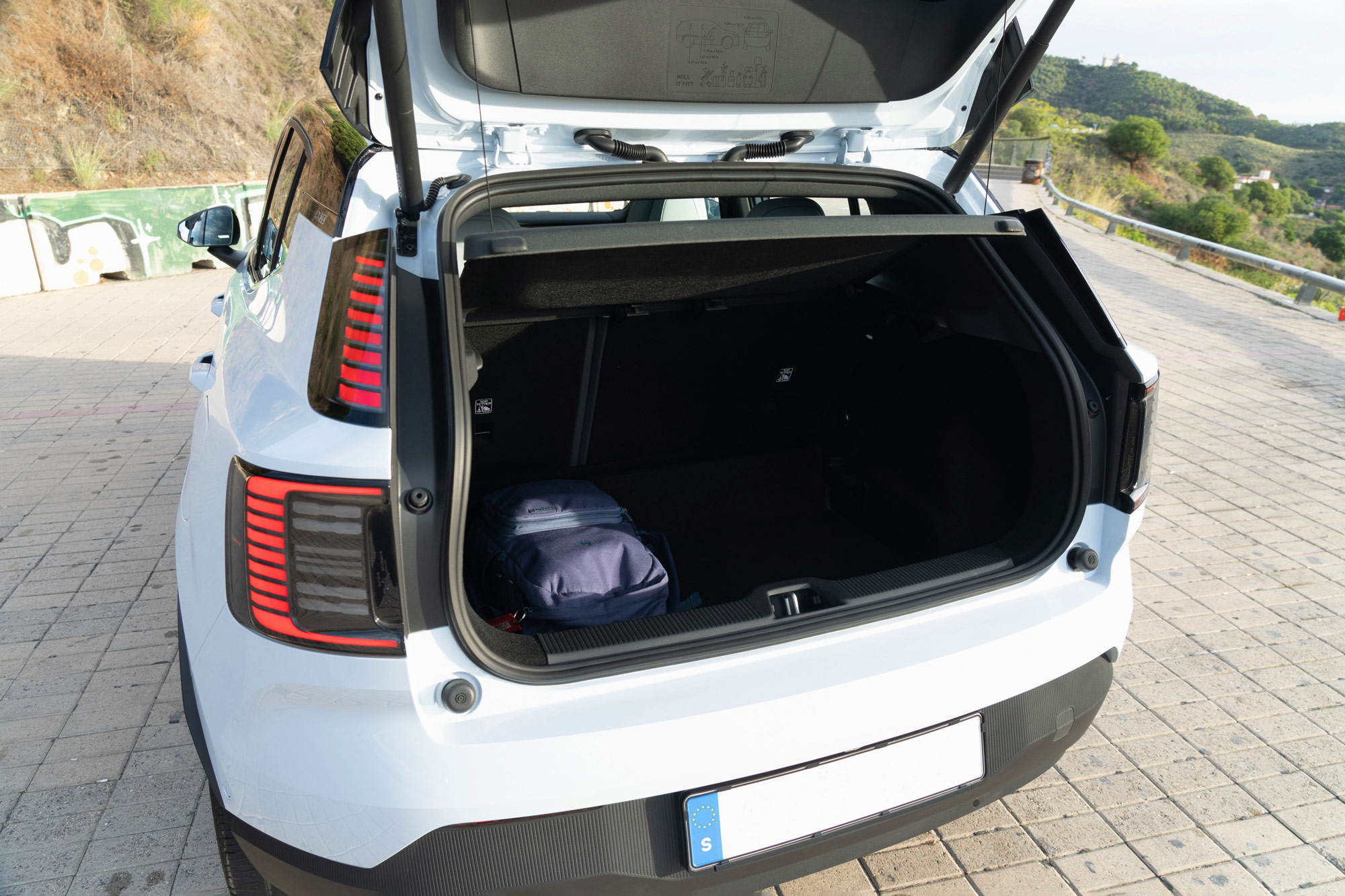 White 2025 Volvo EX30 with rear hatch open and backpack stowed in storage area.