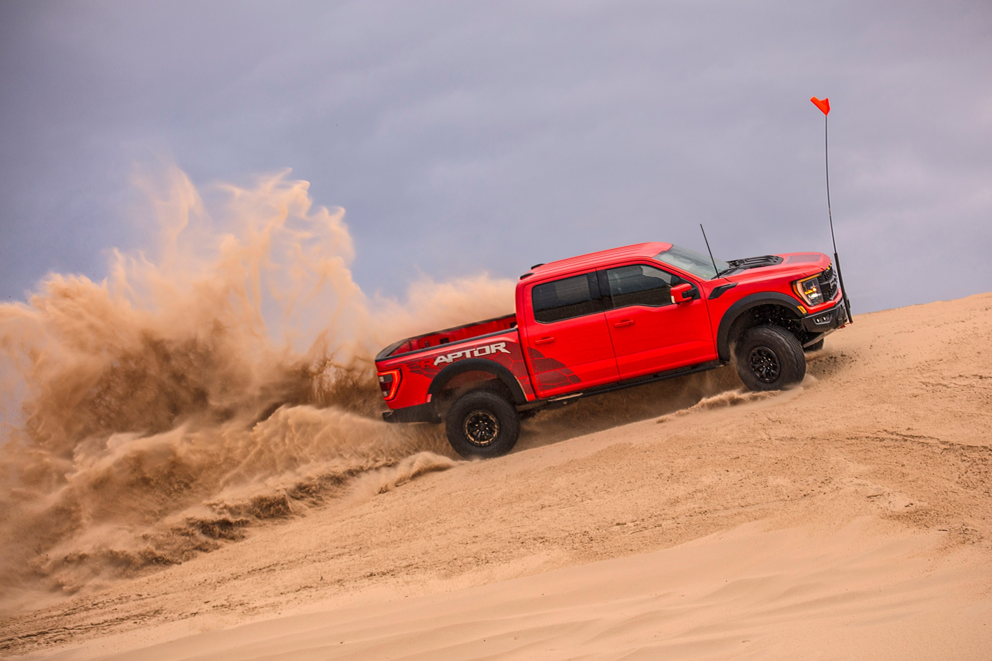 Side view of a red 2023 Ford F-150 Raptor R kicking up sand