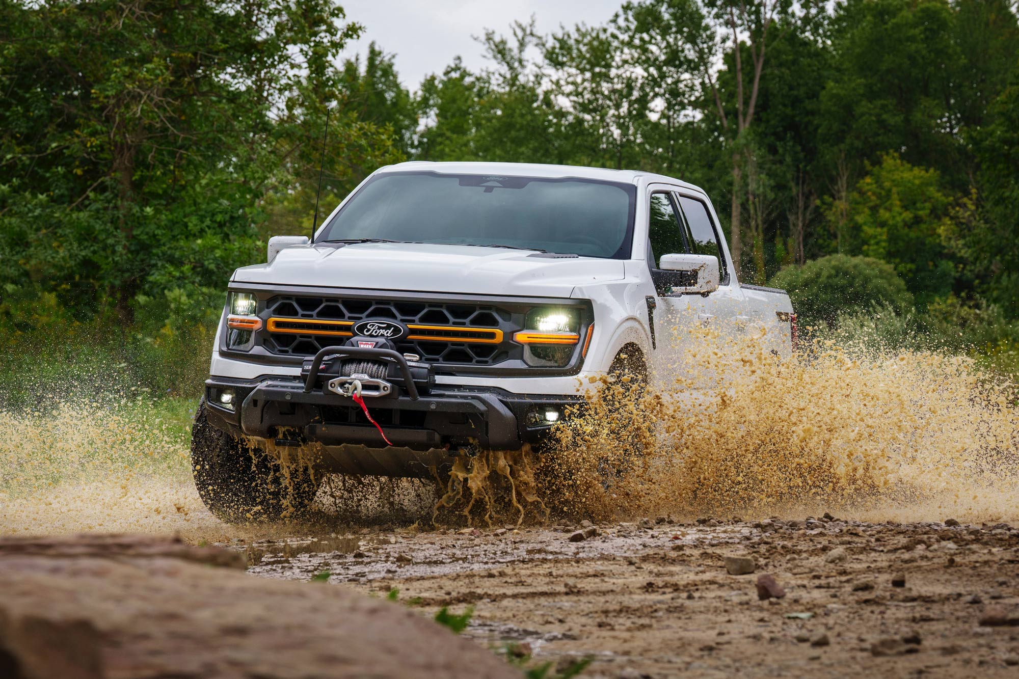 White 2024 Ford F-150 Tremor splashes through a mud puddle off road.
