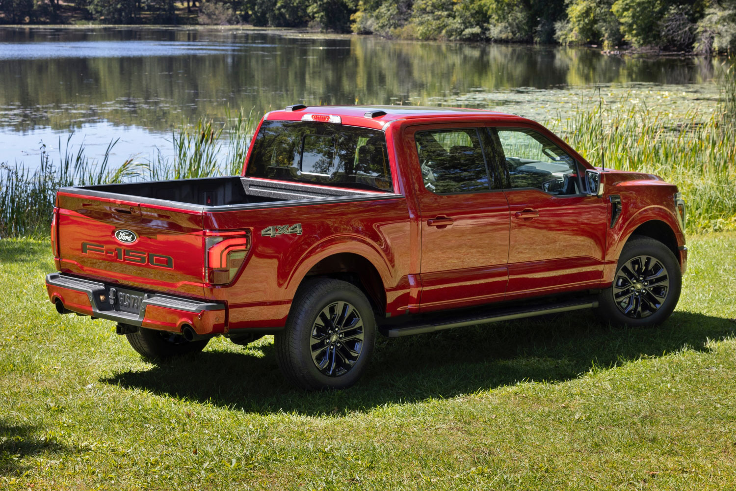 Red 2024 Ford F-150 Lariat parked on grass by a lake.