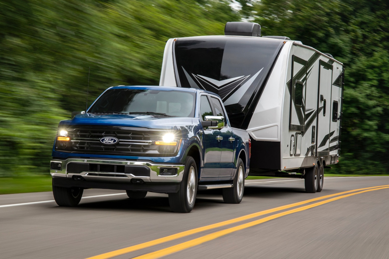 2024 Ford F-150 XLT in blue towing a travel trailer on two-lane road.