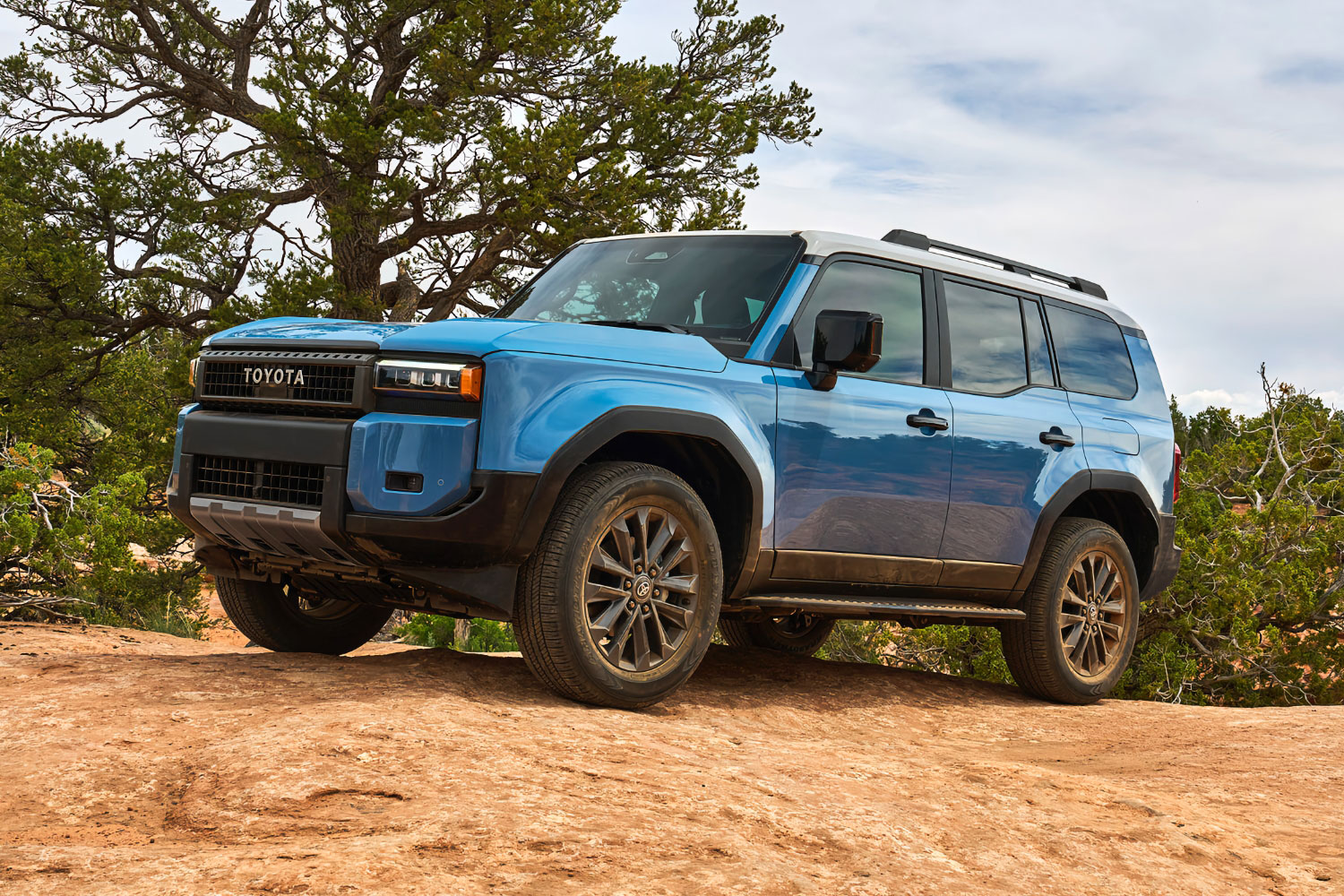 2024 Toyota Land Cruiser in Heritage Blue with white roof parked on rocky ground.