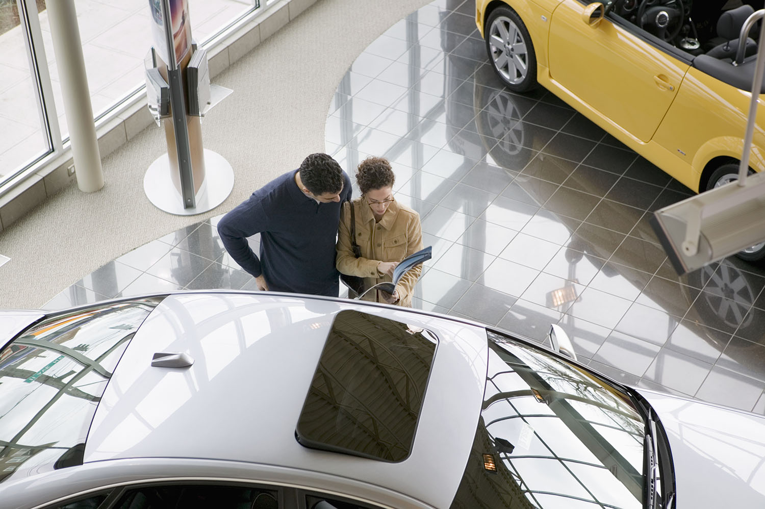 Two people look at car and brochure in dealership