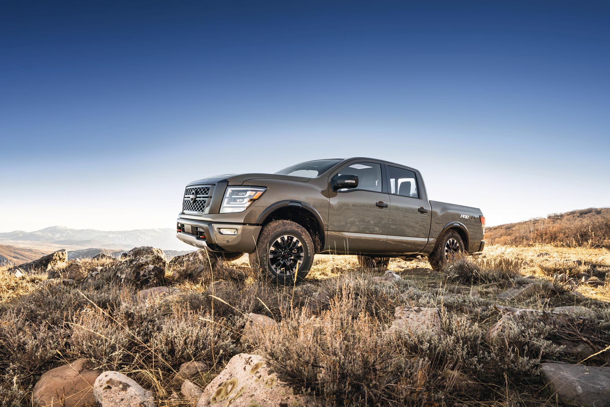 2023 Nissan Titan sits parked off road in a badlands landscape overlooking distant mountains.