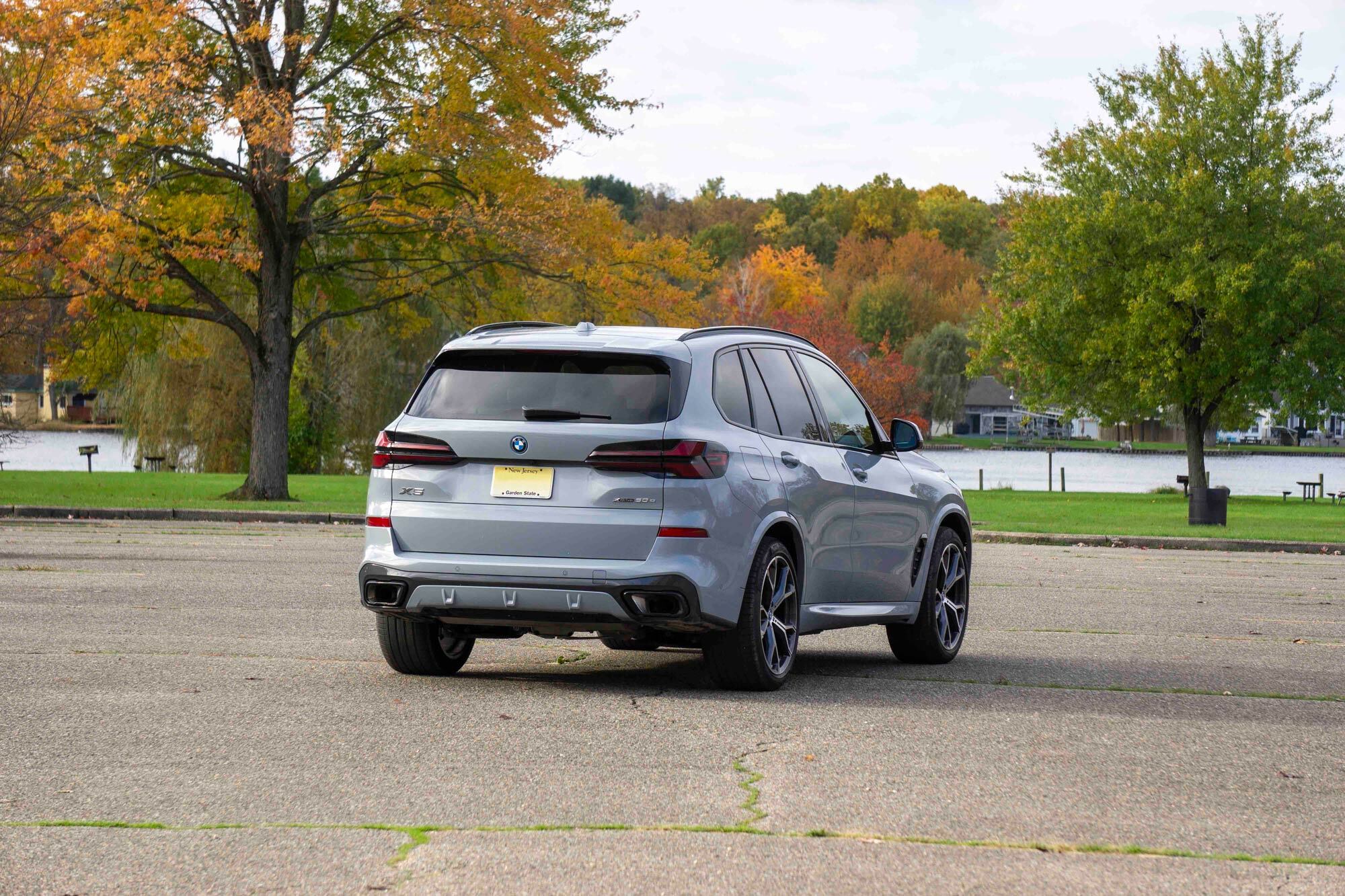 Grey 2024 BMW X5 xDrive50e rear view parked by lake and trees