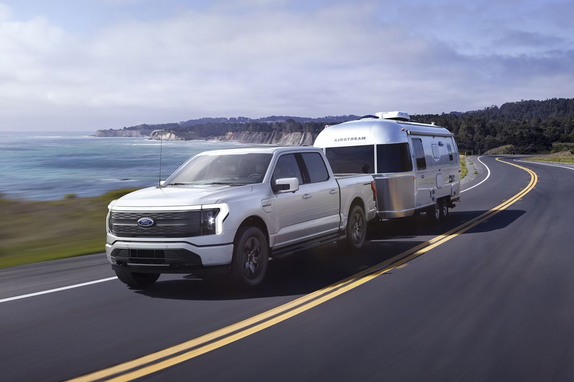 Gray Ford F-150 Lightning pulling an Airstream down the highway next to the ocean