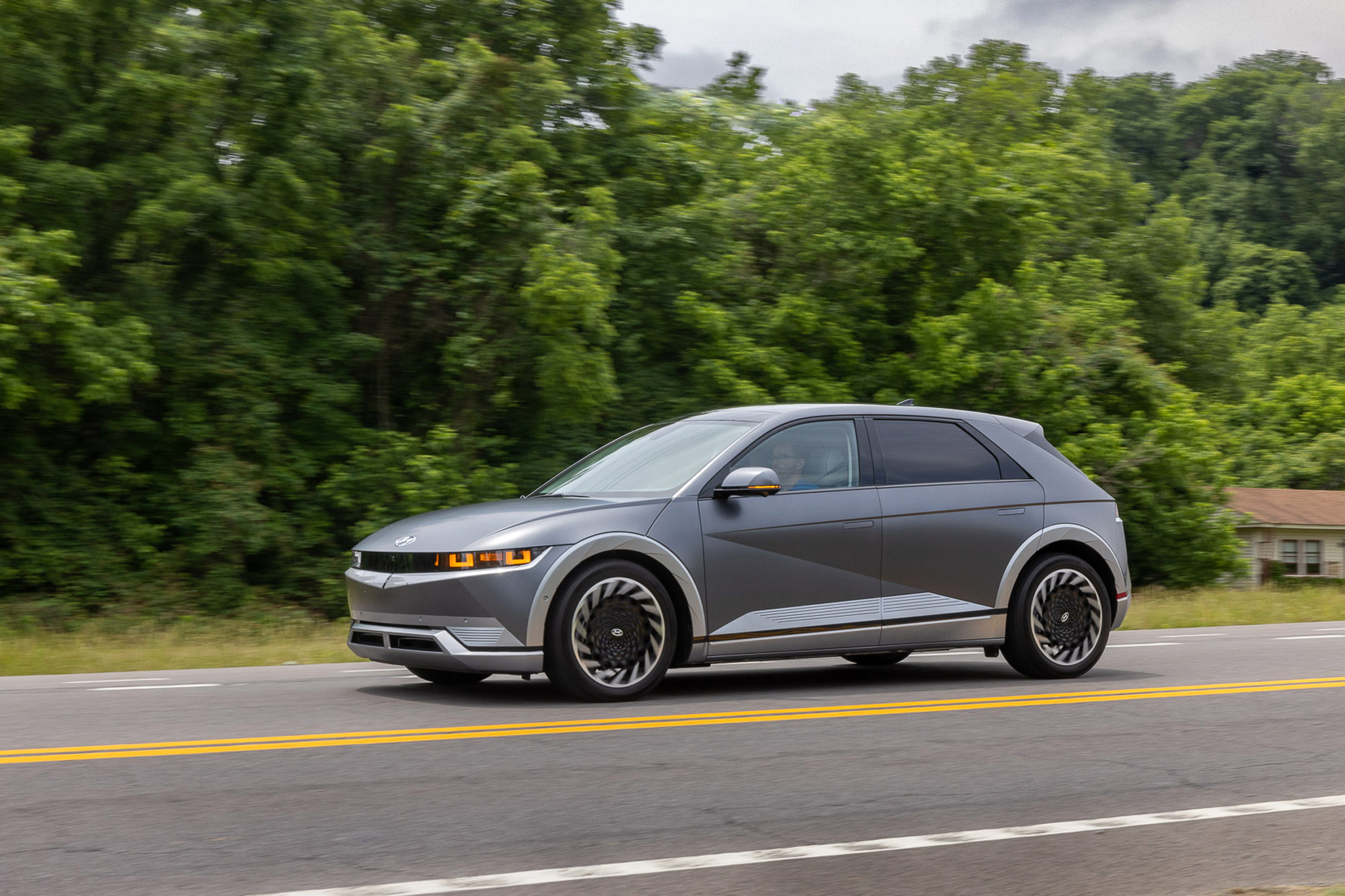 Gray Hyundai Ioniq 5 driving down highway by trees