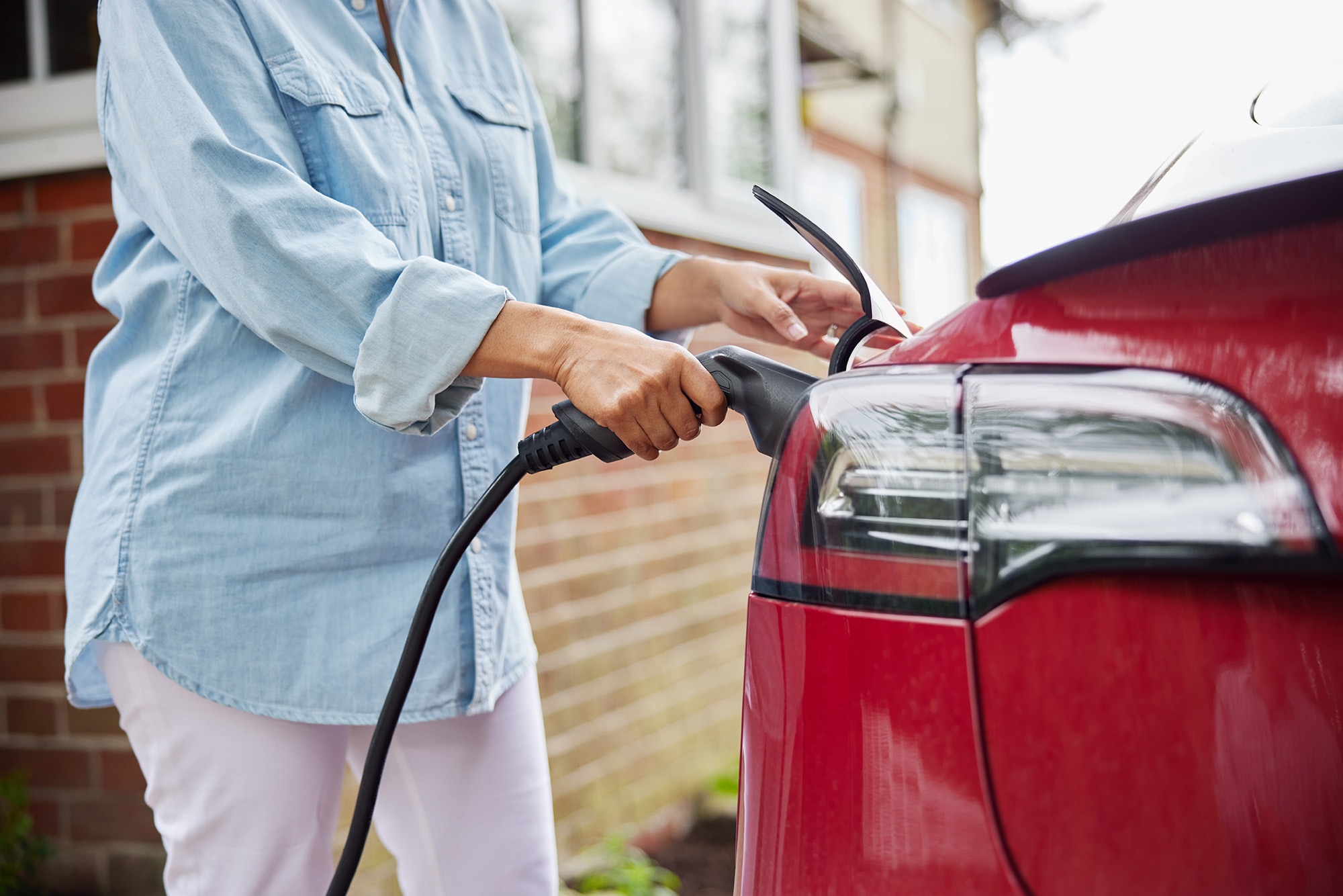 A person attaches a charging cord to an electric vehicle.