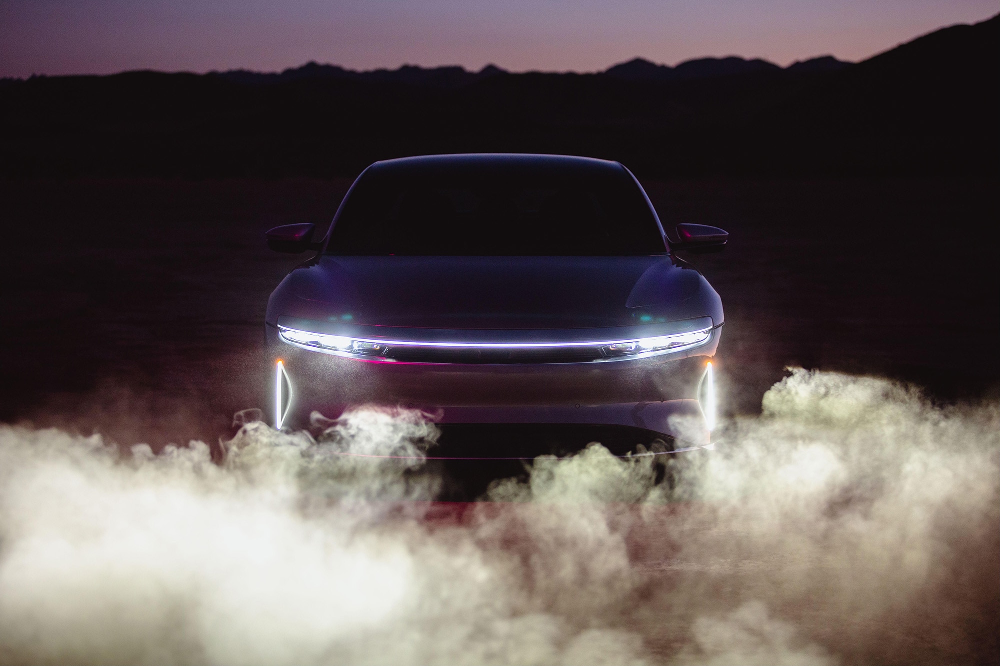 An electric car shines its headlights through a cloud of dust.