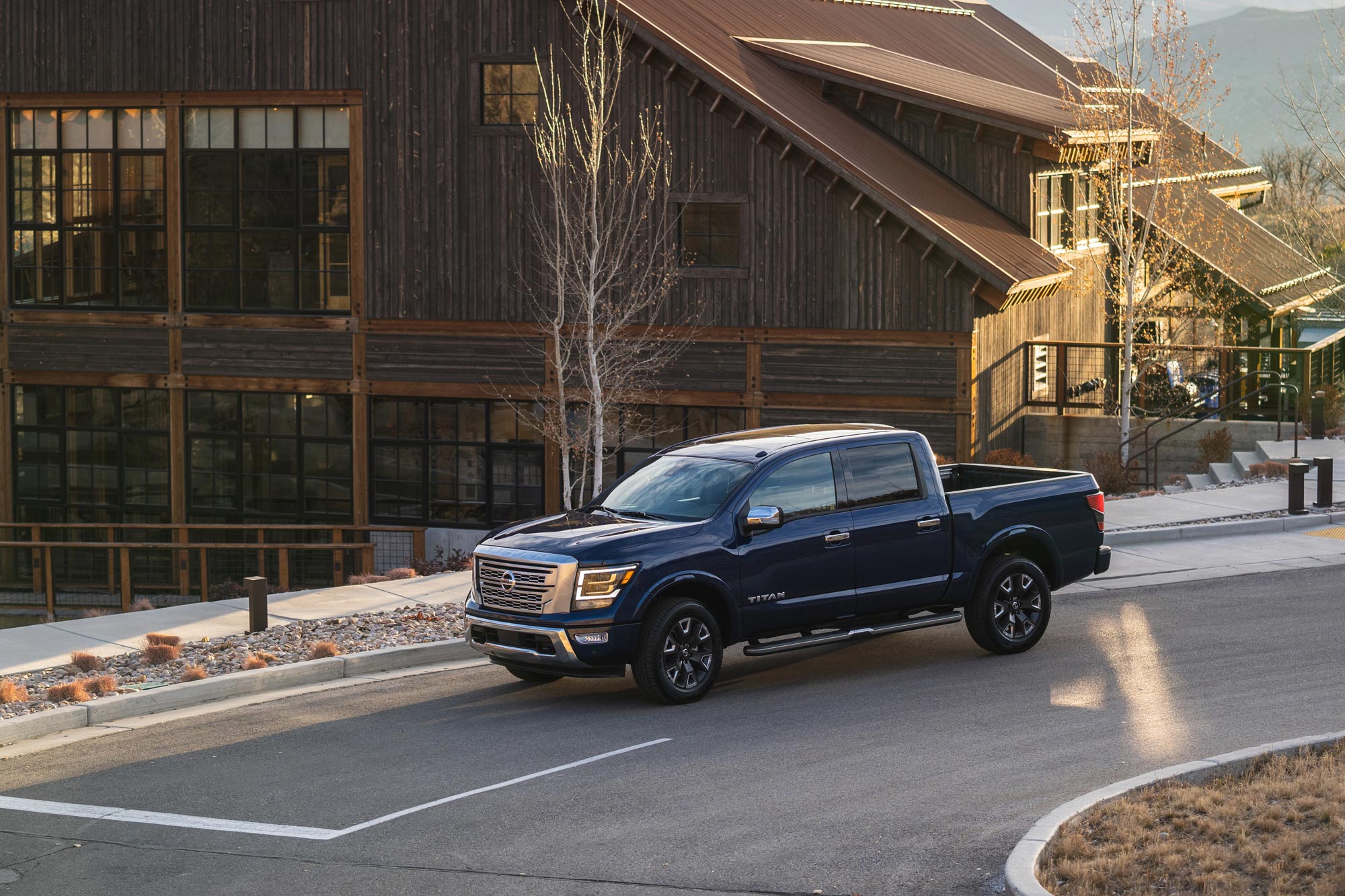 Blue 2023 Nissan Titan sits parked on a road by a large wood sided building.