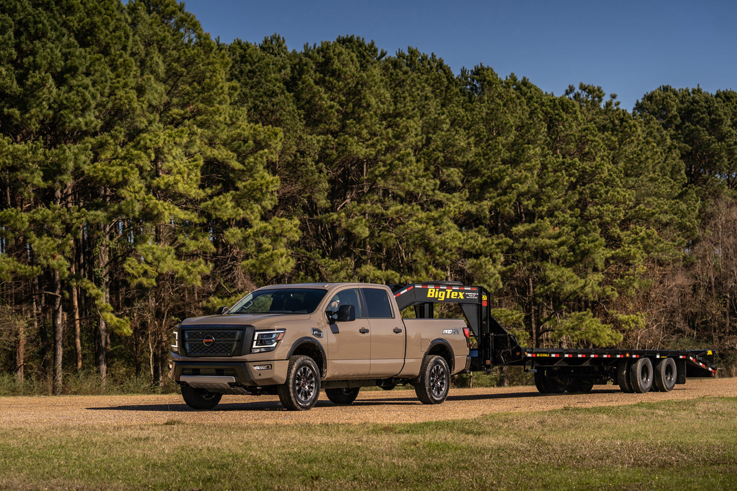 2023 Nissan Titan XD with a fifth-wheel trailer parked on a dirt road by some trees.